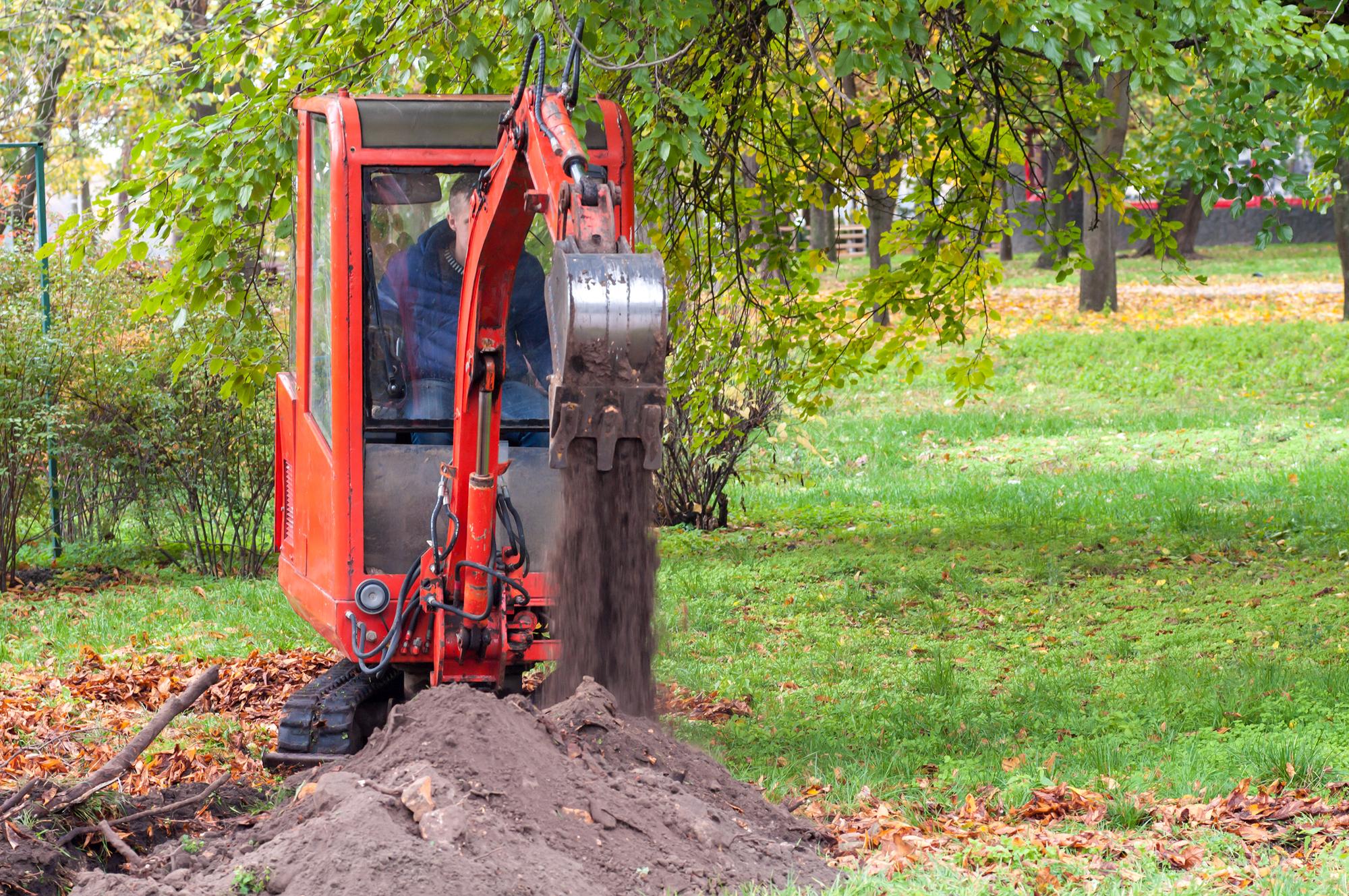 small crawler loader digs in the park trench for laying pipes